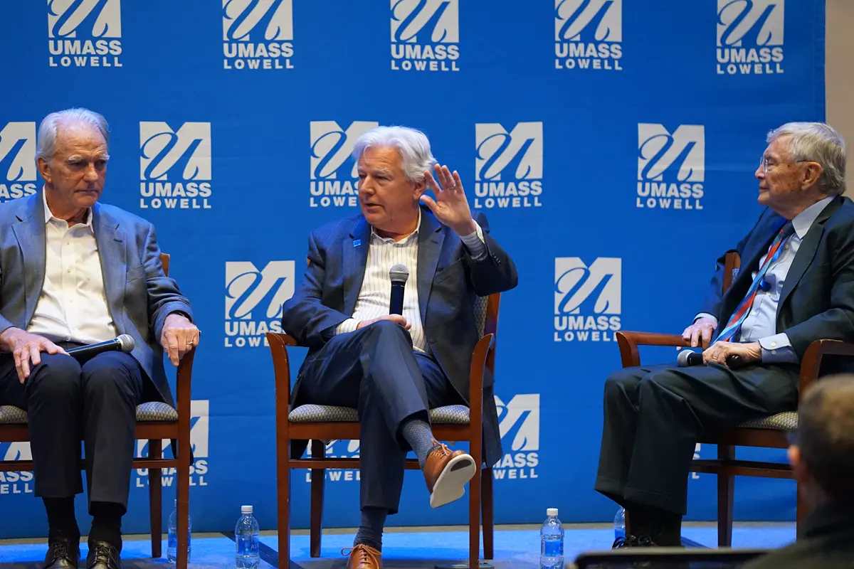 A man gestures with his hand while sitting between two other men on a stage.