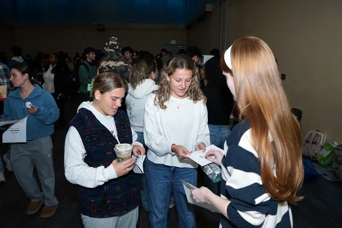 A young woman places a sticker on a person's pamphlet while standing next to another person.