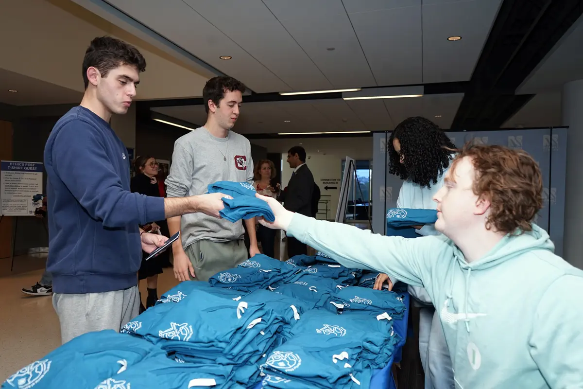 A young man hands a blue T-shirt to a person at a table.