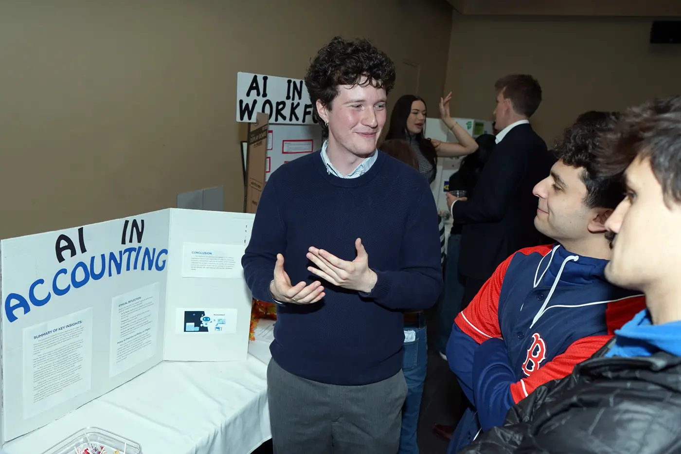 A young man in a dark sweater talks about a poster presentation with two other young men.