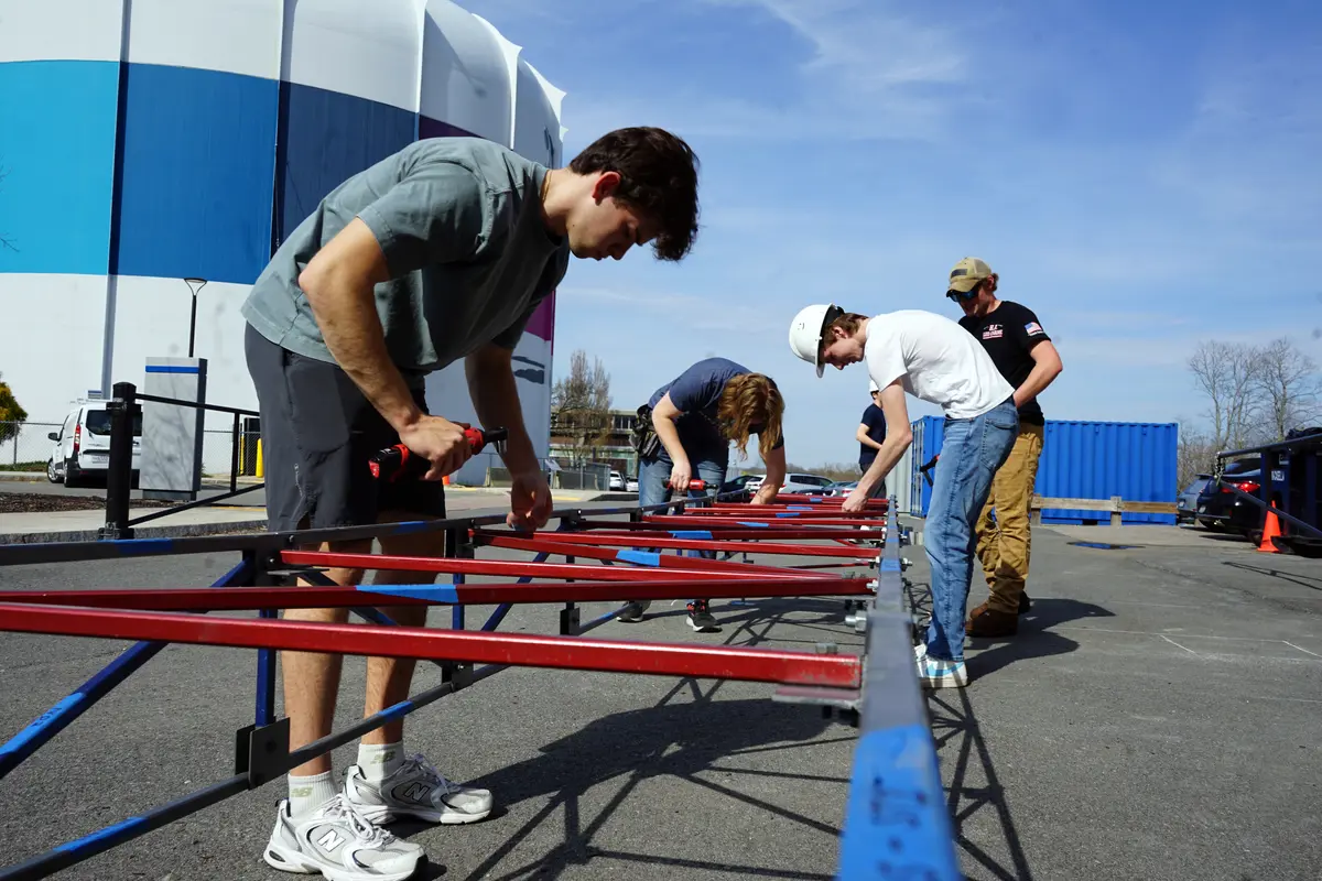Four college students work on building a steel bridge in a parking lot.