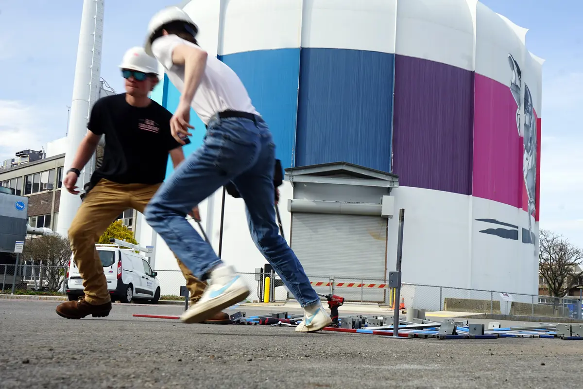 Two young men in hardhats start running outside in front of a nuclear reactor.