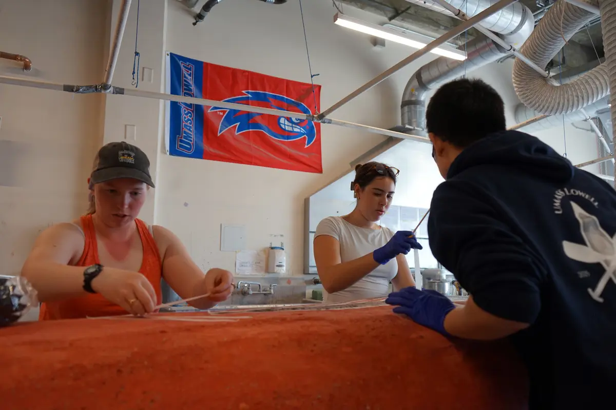 Three college students work on decorating a concrete canoe in a garage bay.