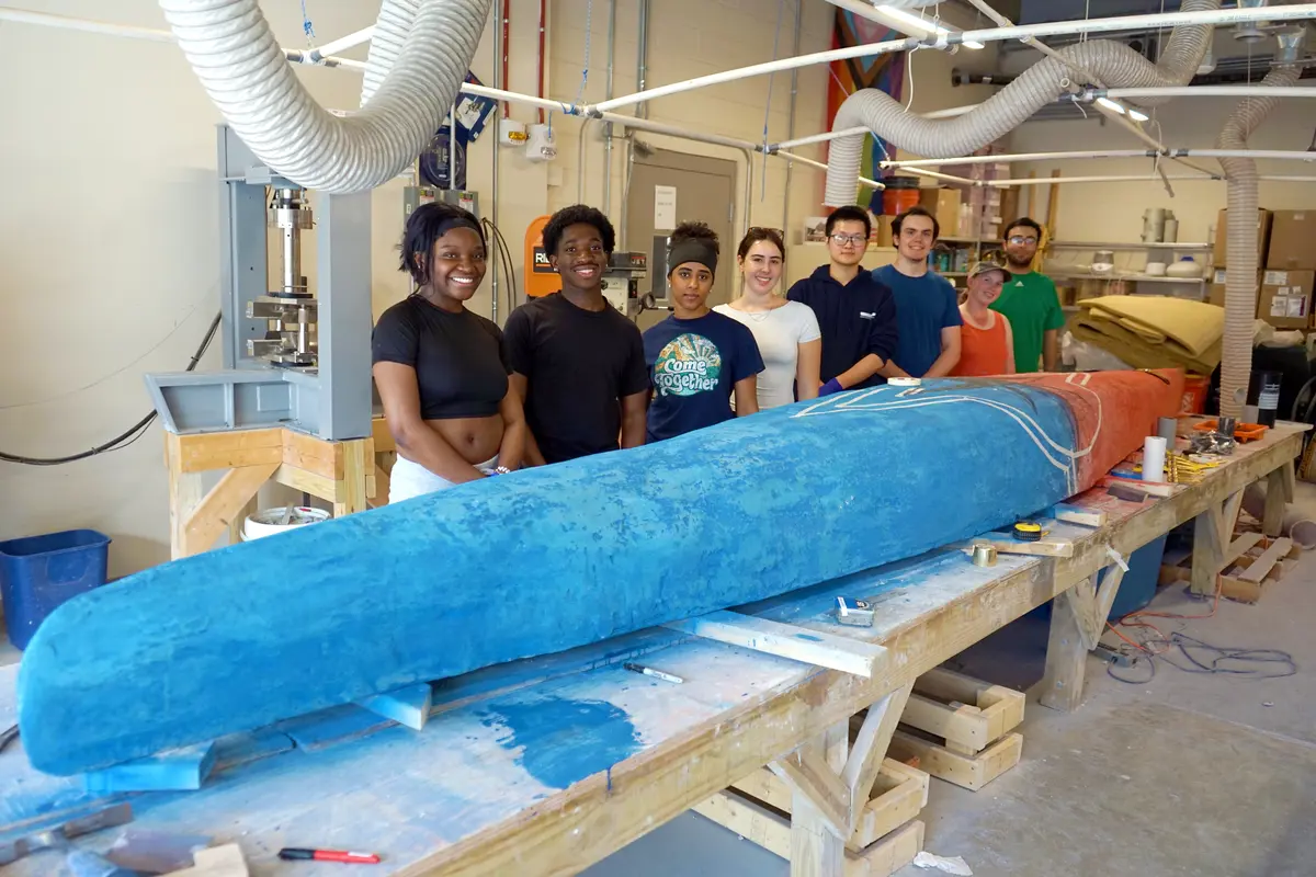 Eight college students pose with a concrete canoe inside a garage bay.