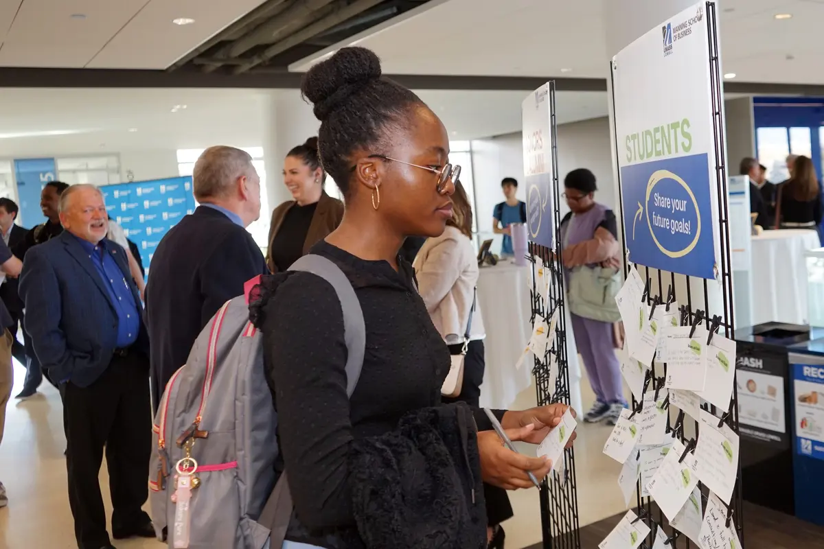 A young woman looks to add a note to a stand with other notes in the foyer of a building.