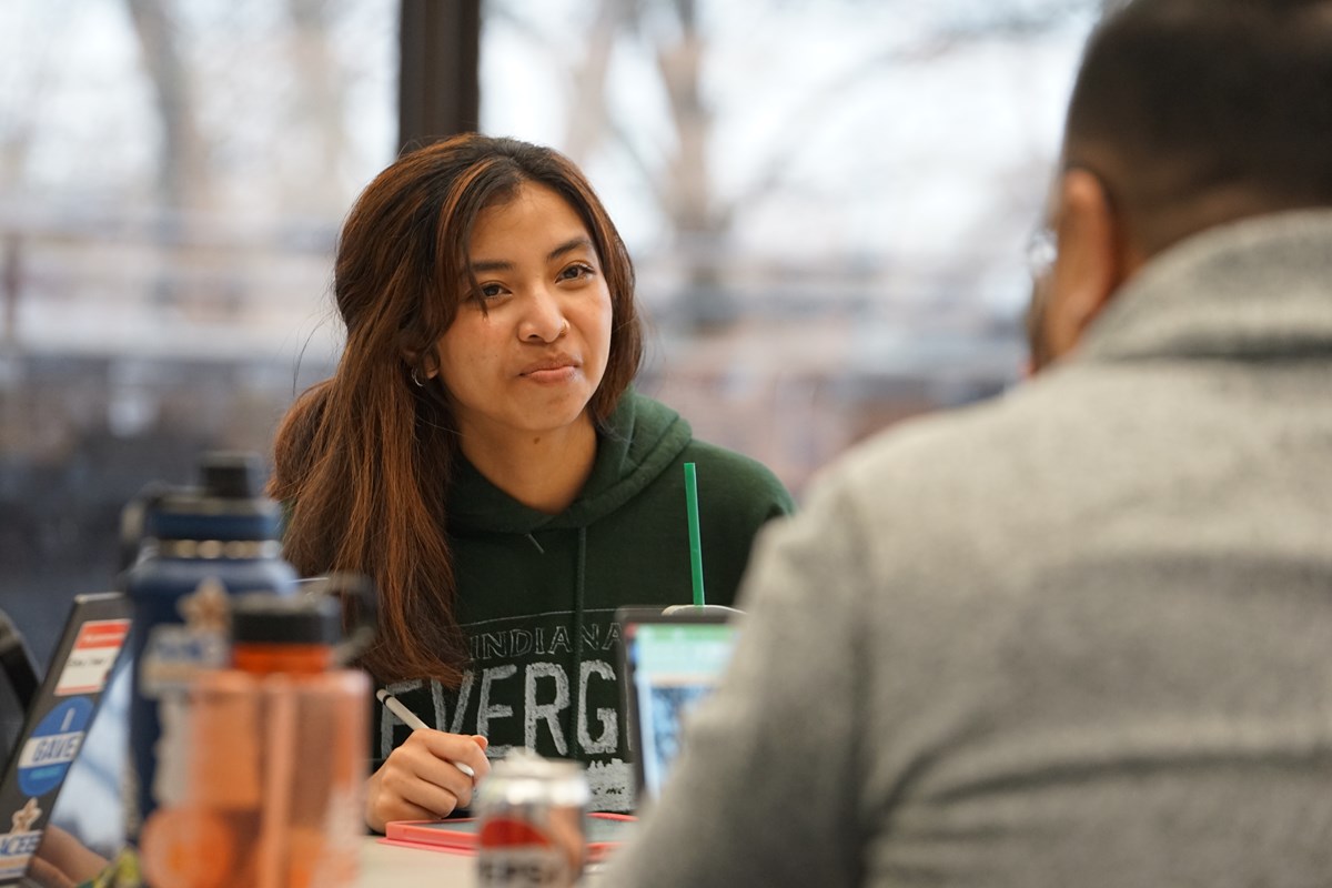 A person in a green hoodie smiles while looking at a person across a table.