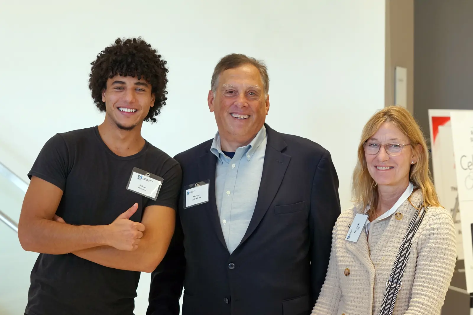 A college student in a black t shirt poses for a photo with a man and a woman.