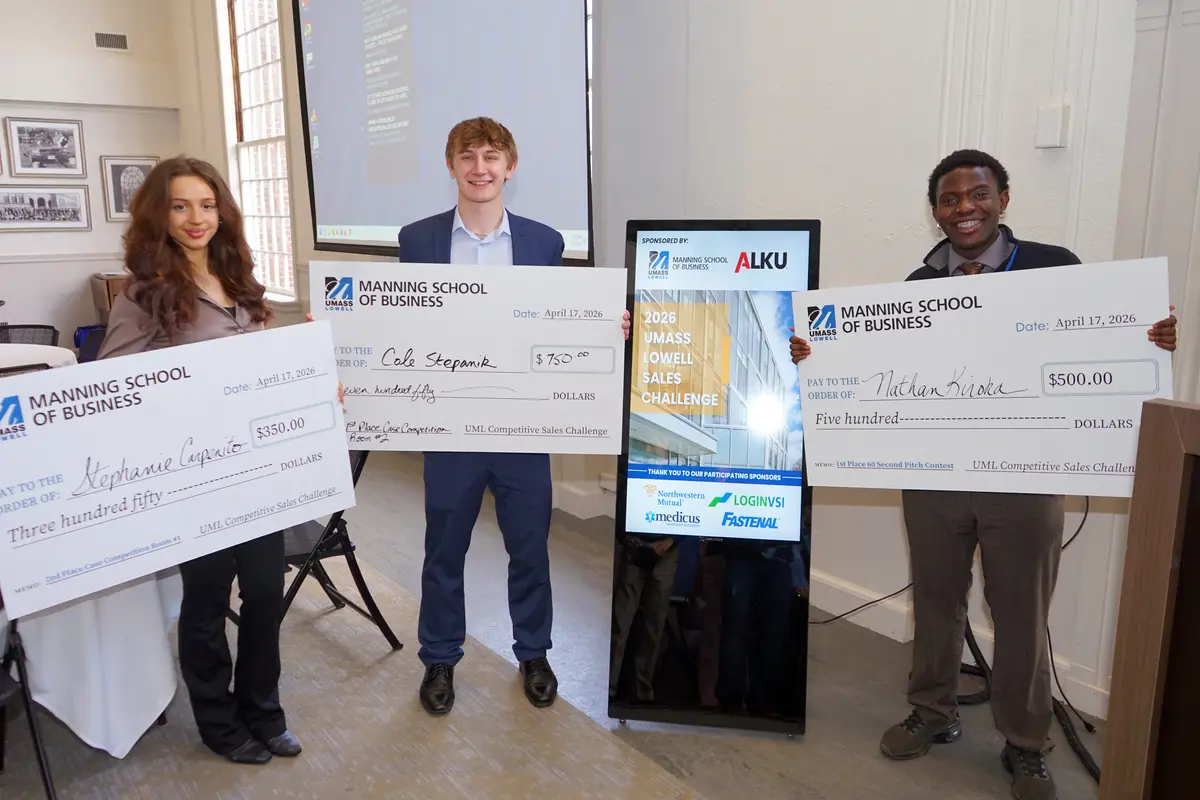 A young woman and two young men pose for a photo while holding oversized checks.
