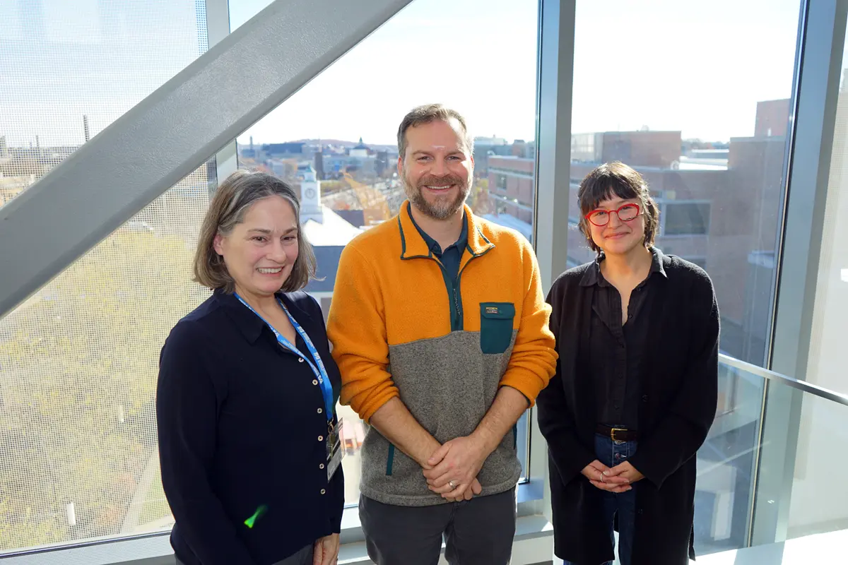 Two women and a man pose for a photo in front of a window.