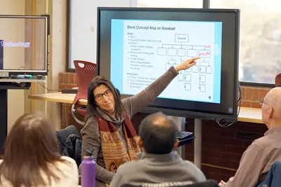 A man in a checkered shirt uses a touch screen monitor in a classroom.