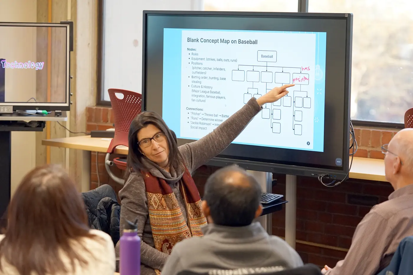 A woman points to a touch screen in a classroom while three people look at her.