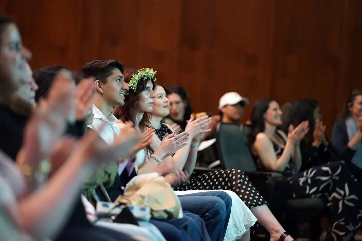 A row of people applaud in a theater.