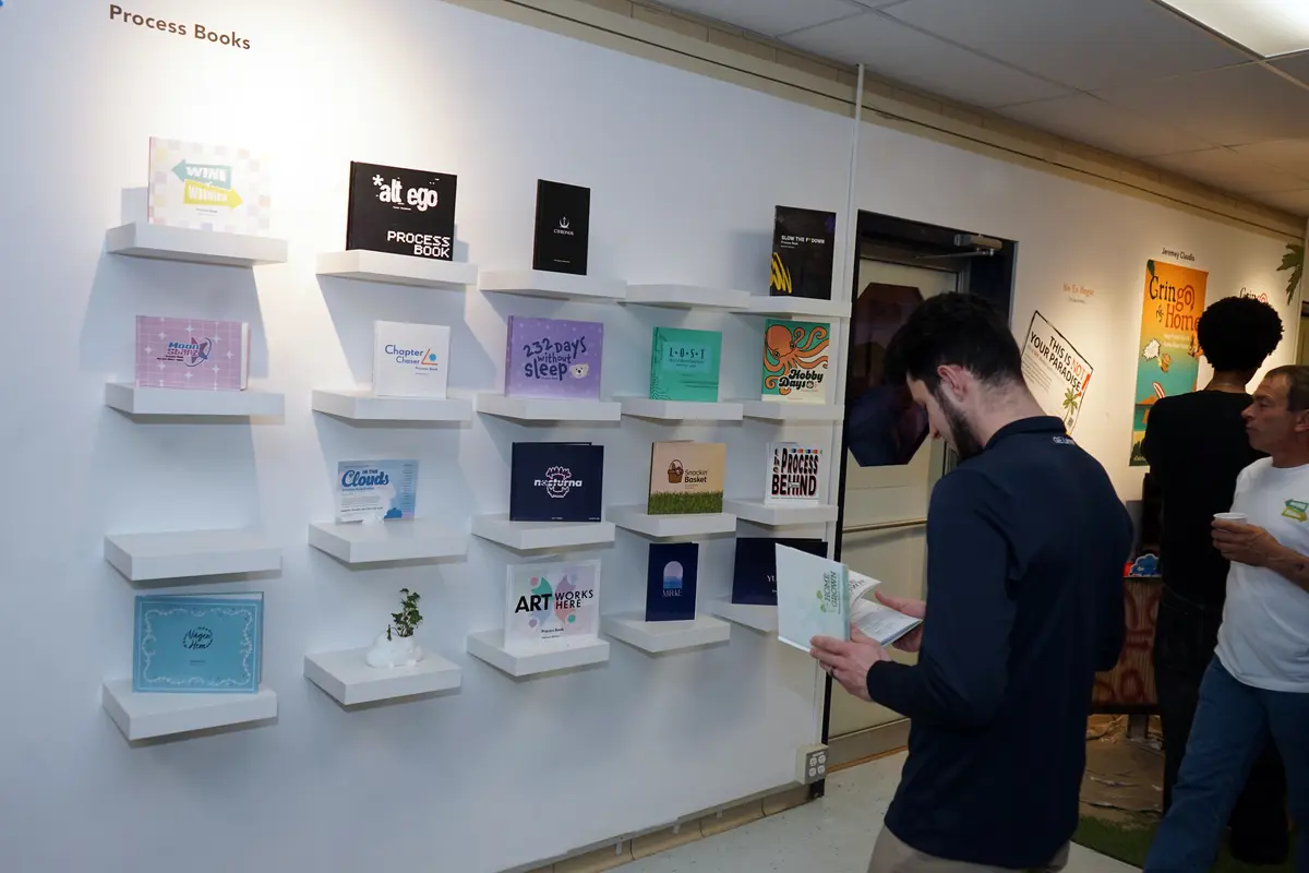 A man looks at a book in front of a wall display with 20 other books.