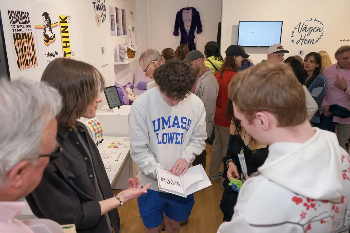 A young man looks at a book while other people look on in a crowded art exhibit room.