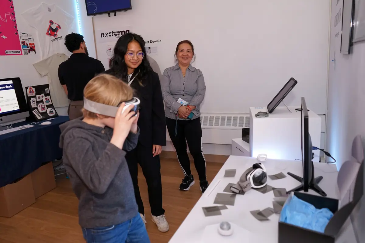 A youngster wears goggles while looking at a screen while two women look on at an art exhibit.