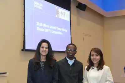 Three students pose in front of a Three Minute Thesis Competition sign.