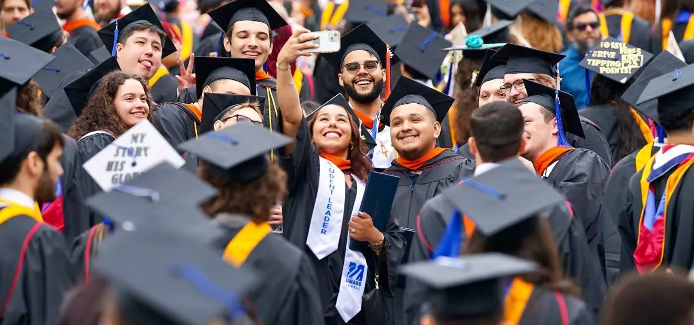 Woman taking selfie amid dozens of graduates in black graduation gowns and mortarboards