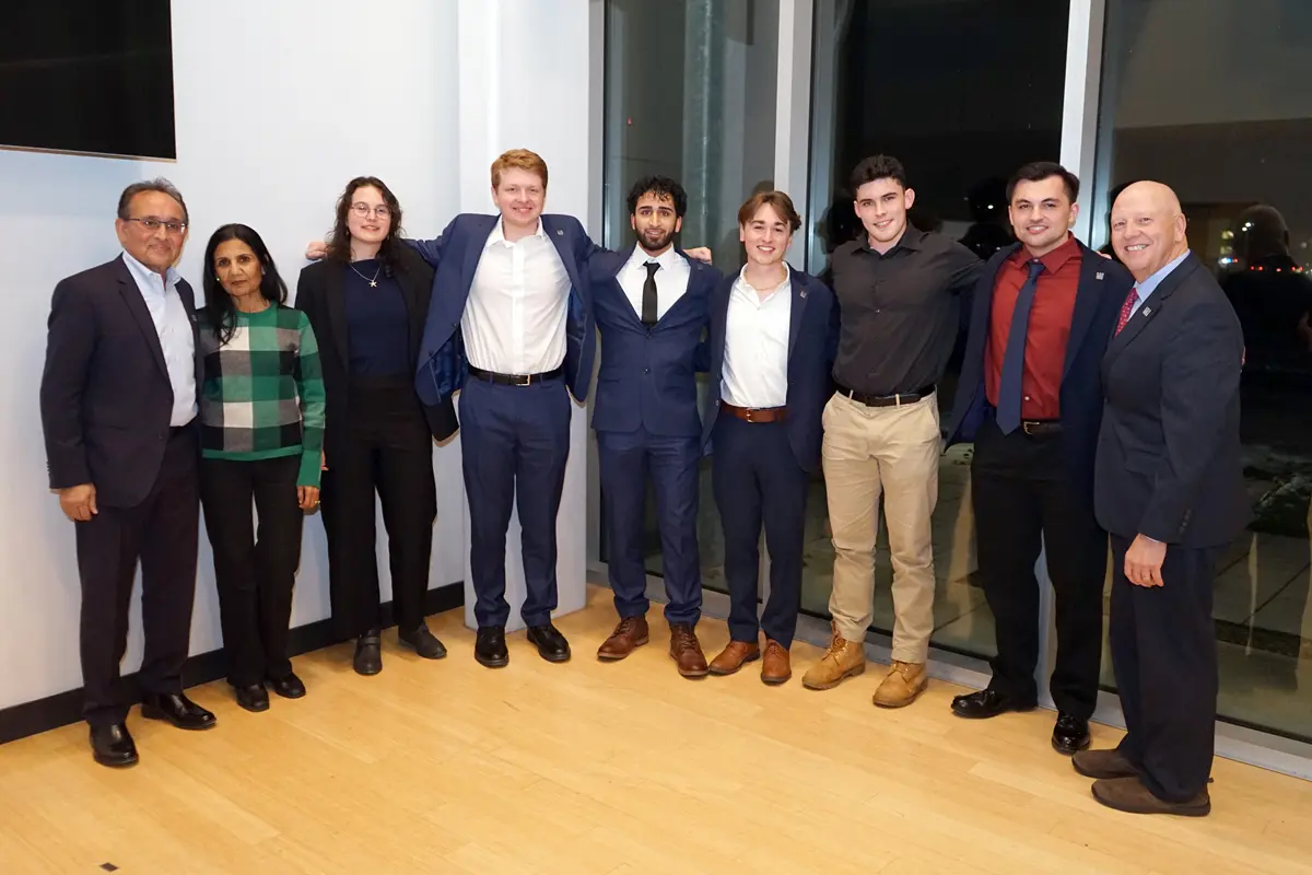 Nine people pose for a group photo while standing in the corner of a room.