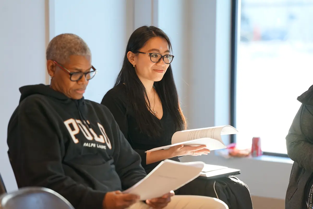 Two women with glasses react while looking at papers.