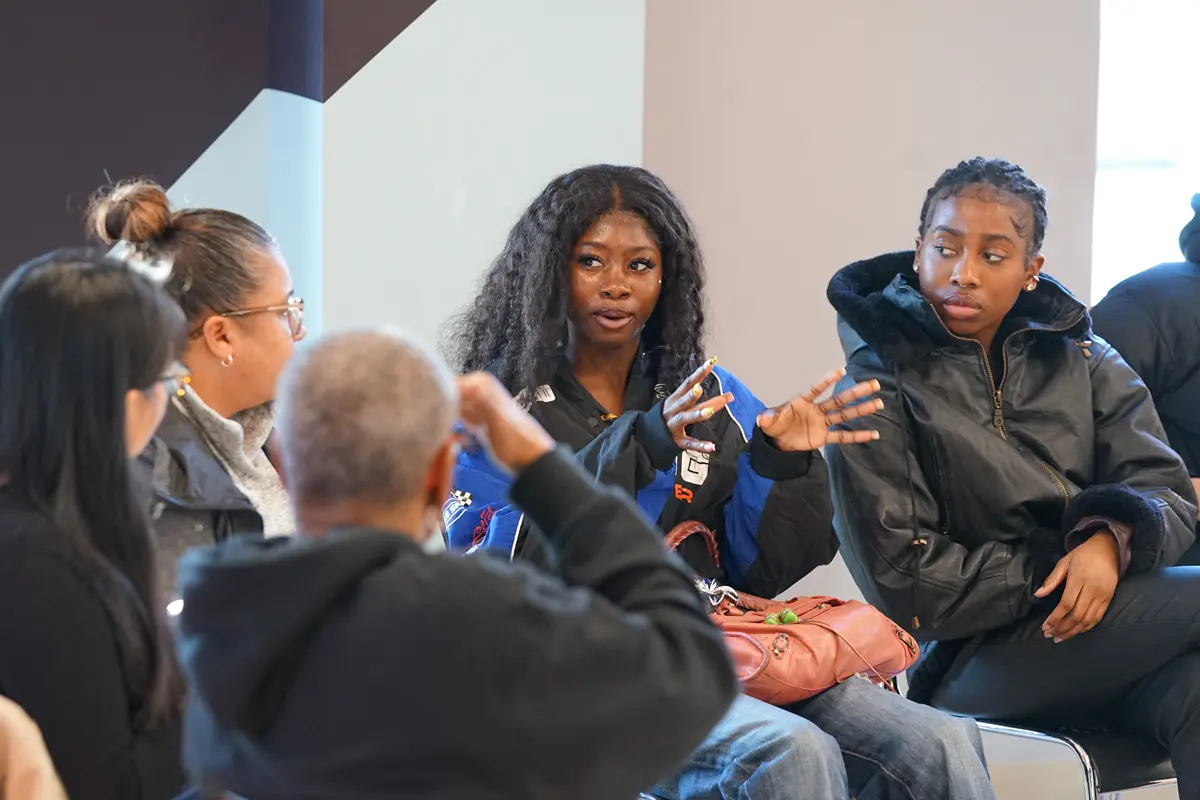 A man in a vest talks to a group of students outside a building while a man holds the door open.