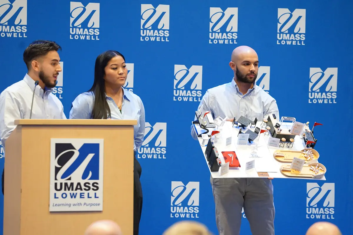 A man holds a model of an entertainment center while a man and a woman look on next to a podium.