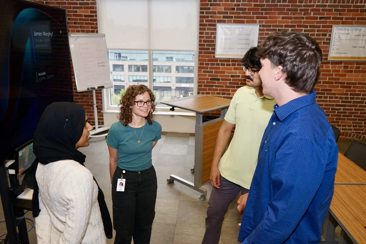 Two young women and two young men stand in a circle and chat in a conference room.