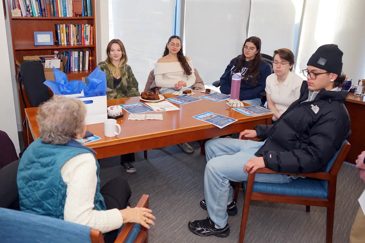 Five college students listen to a woman talk while seated around a table in an office.