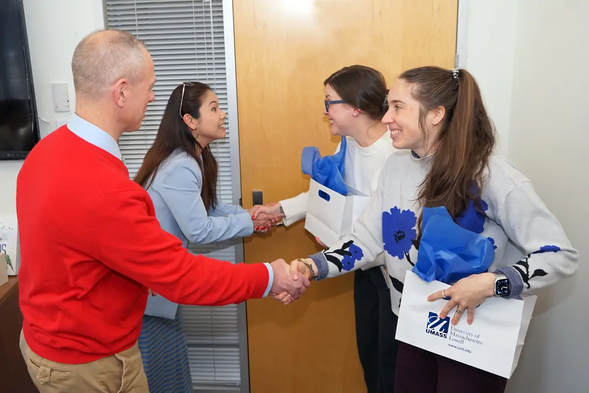 A man and a woman shake hands with two women after handing them gift bags in an office.