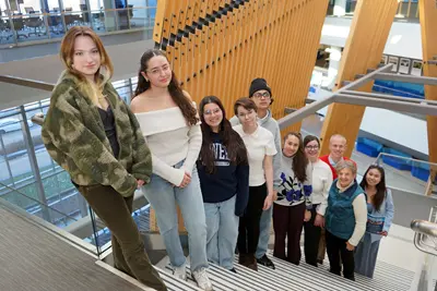 Ten people pose for a group photo while looking up from a staircase in the lobby of a building.