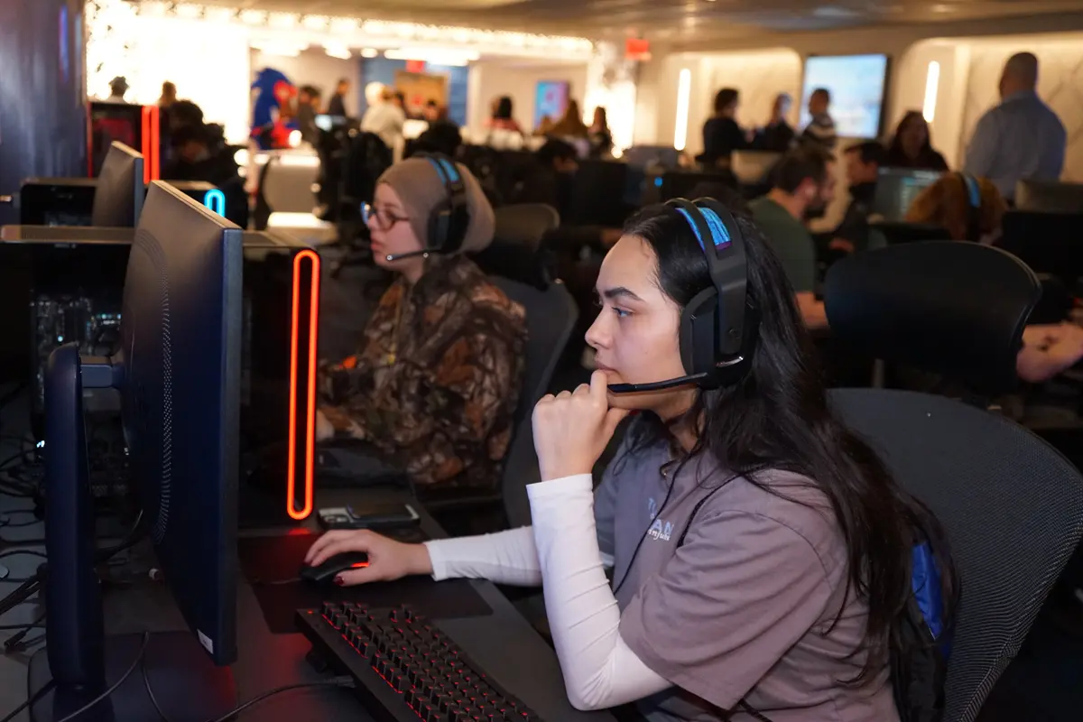 Two young women wear headsets while playing a PC video game in an esports arena.