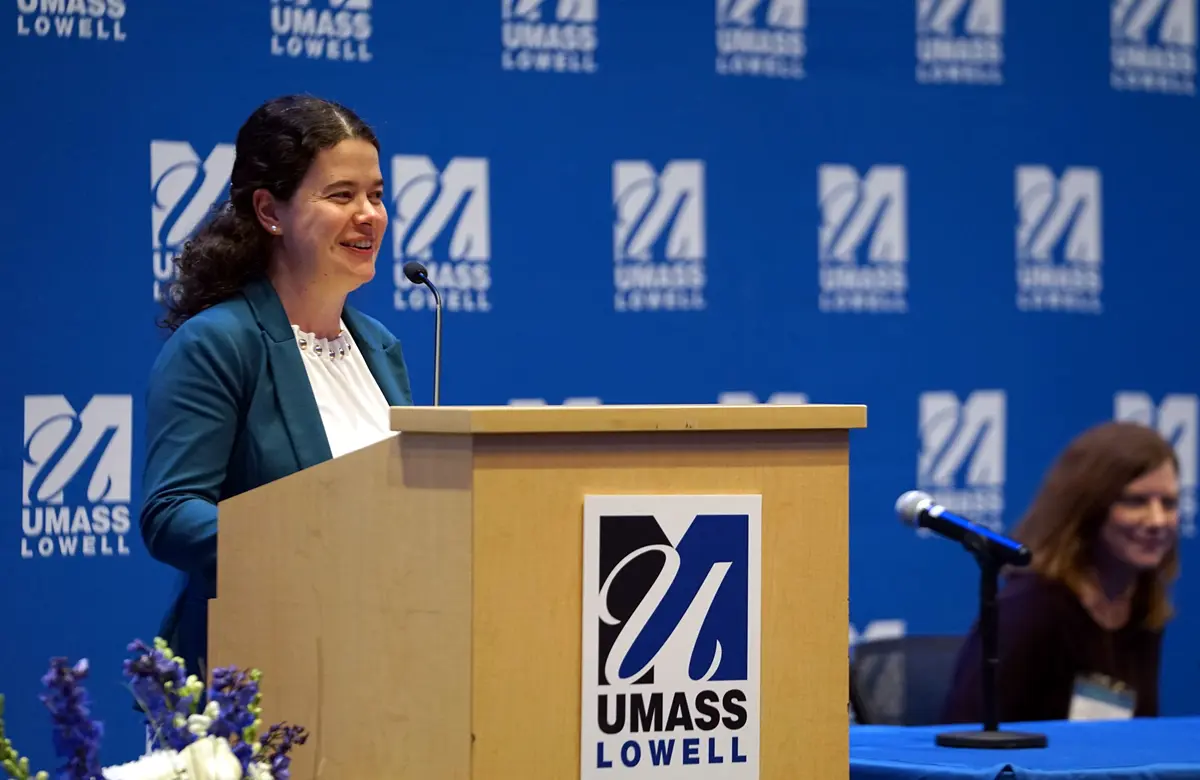 Faculty member standing behind a podium with a UMass Lowell logo backdrop.