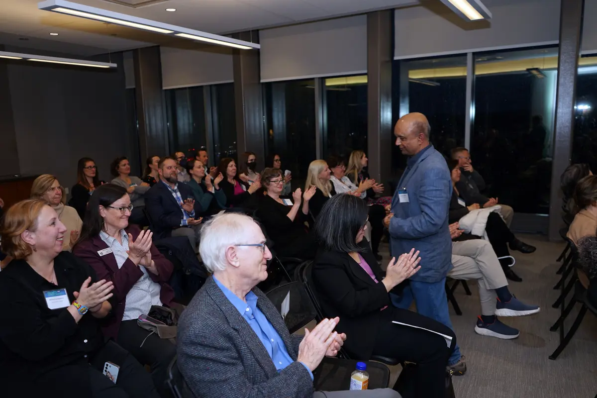 Faculty member standing in a crowd of clapping audience members