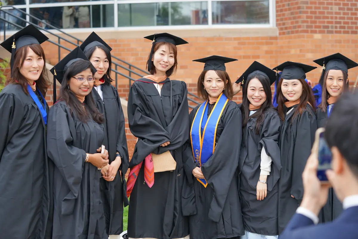 College graduates in black caps and gowns pose for a group photo outdoors.