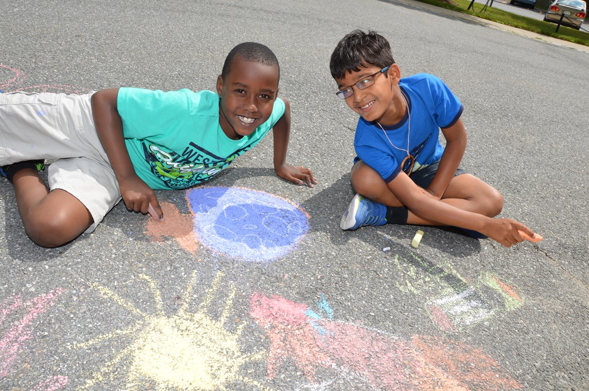 Two young boys draw on sidewalk with chalk
