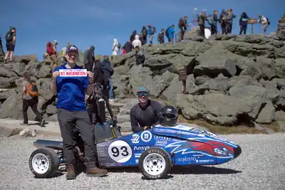 A race car drives on a mountain road, with mountains on the horizon.