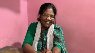 Dayamani Barla smilng and holding her own hands in front of a pink wall.