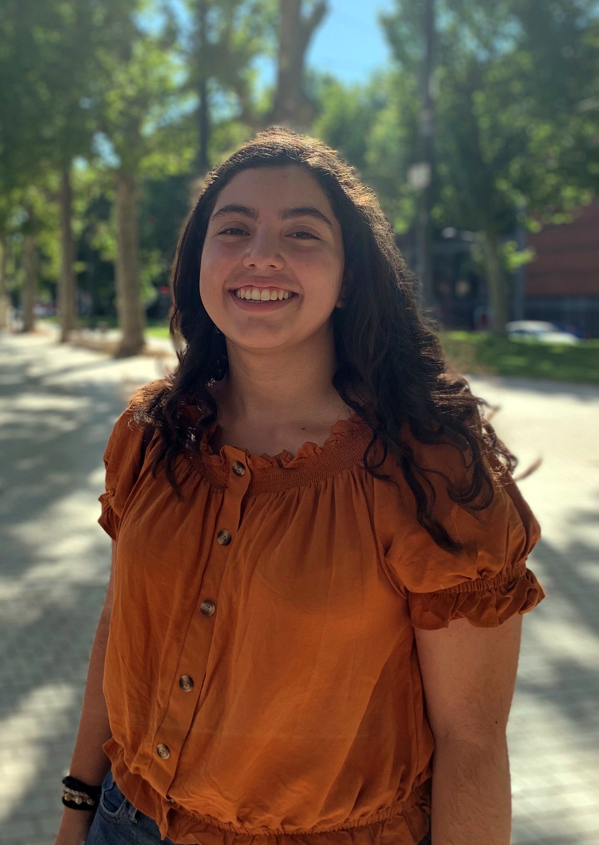 Daniela Salinas Camacho standing outside in an orange shirt smiling at the camera.