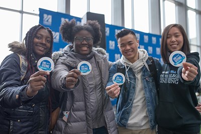 Four smiling students display their Days of Giving stickers