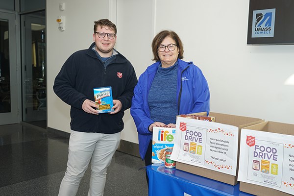 A young man and woman pose for a photo while standing next to food donation boxes