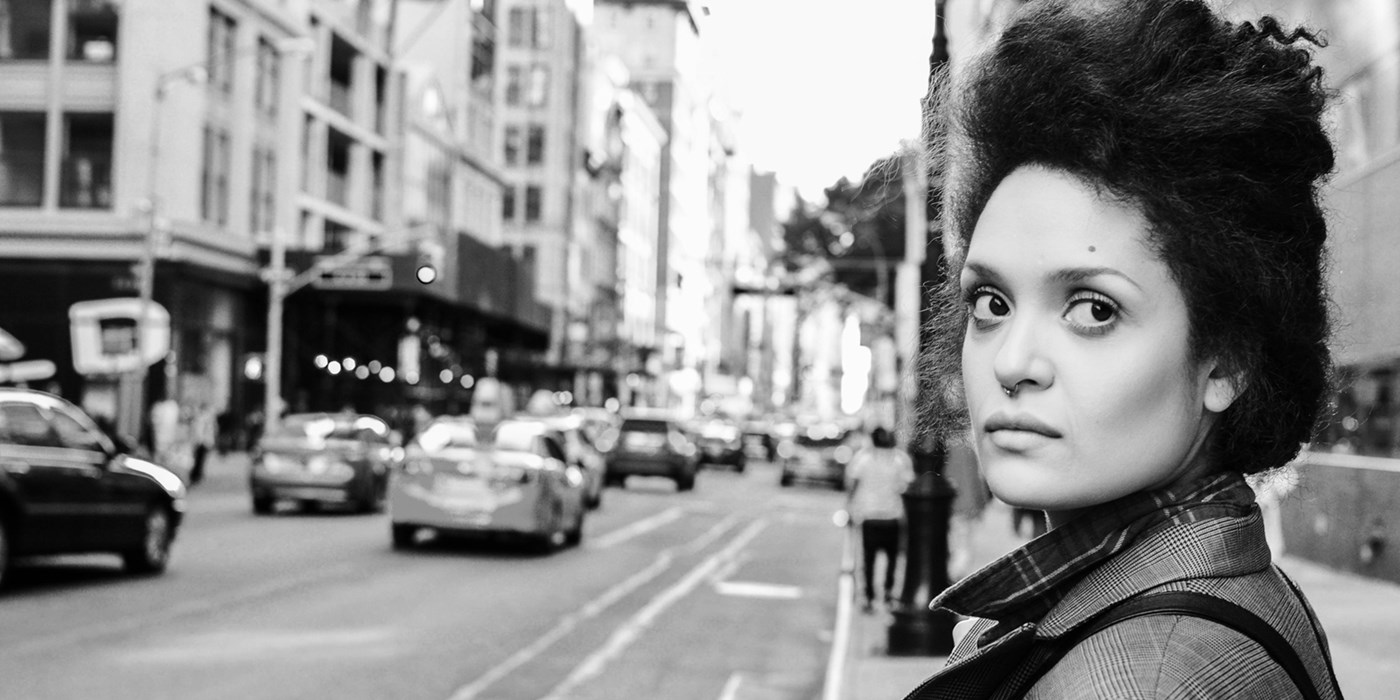 Black & white photo of Diannely Antigua before crossing a street in New York, looking away from the camera