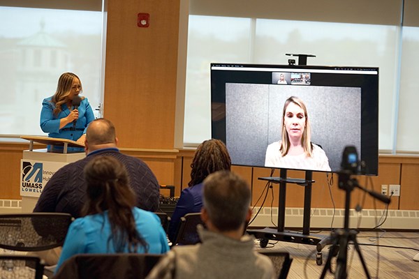 A woman speaks via video conference to people in a room