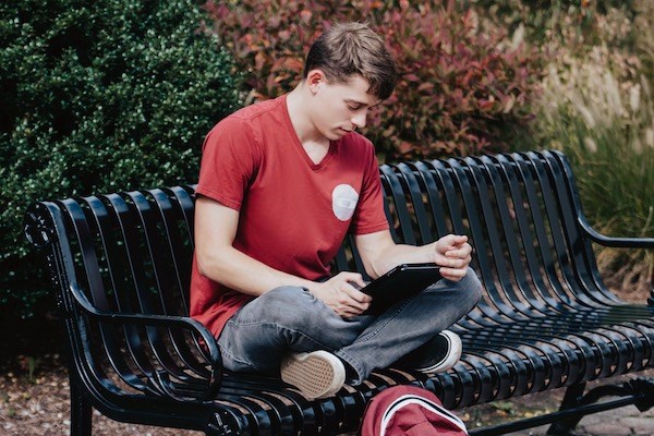 A student reads from a tablet while sitting on a bench
