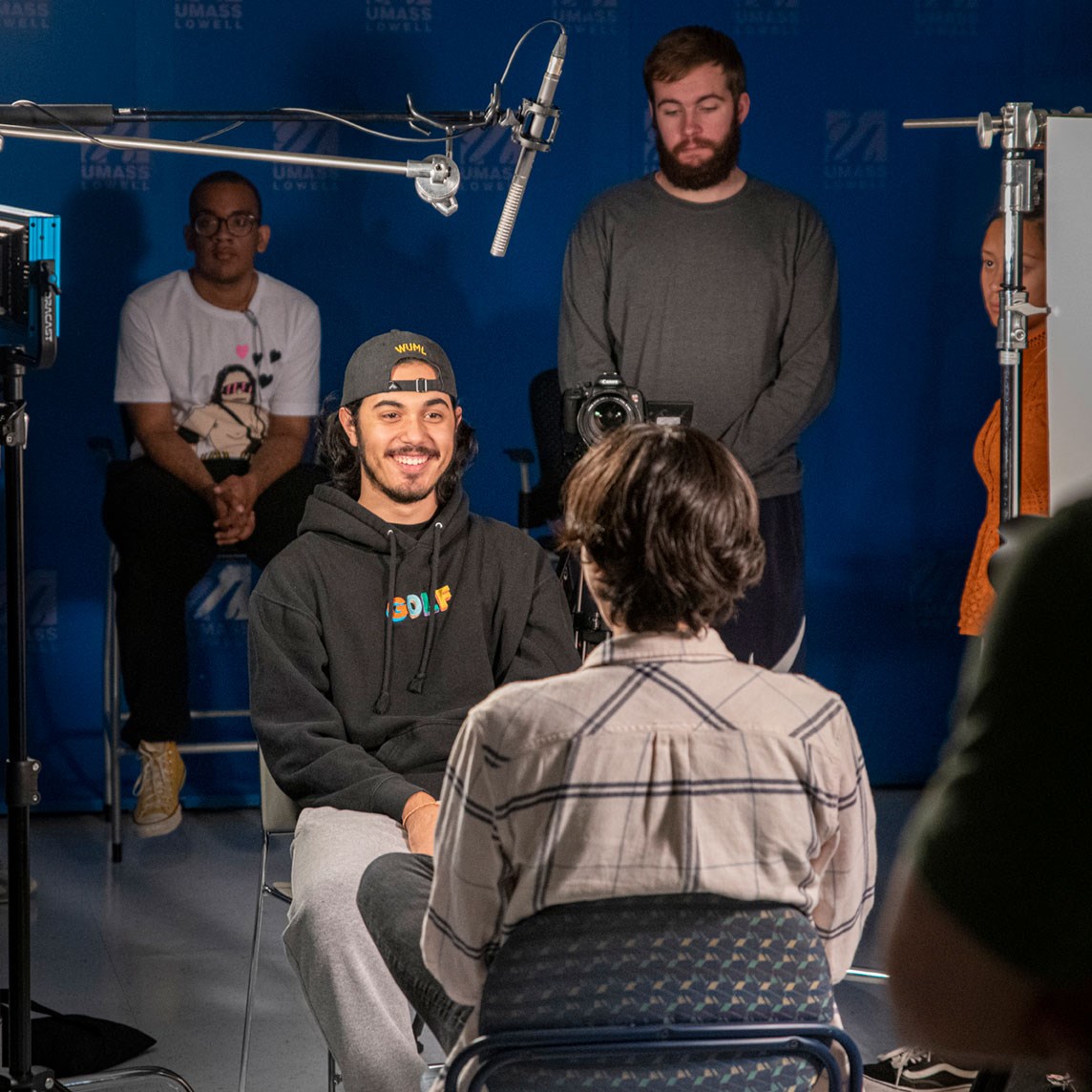 A digital media student is interviewed in a UMass Lowell studio as other students practice videography