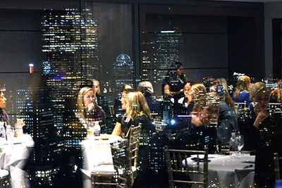 Students are reflected in the UMass Club window with the Boston skyline in the background