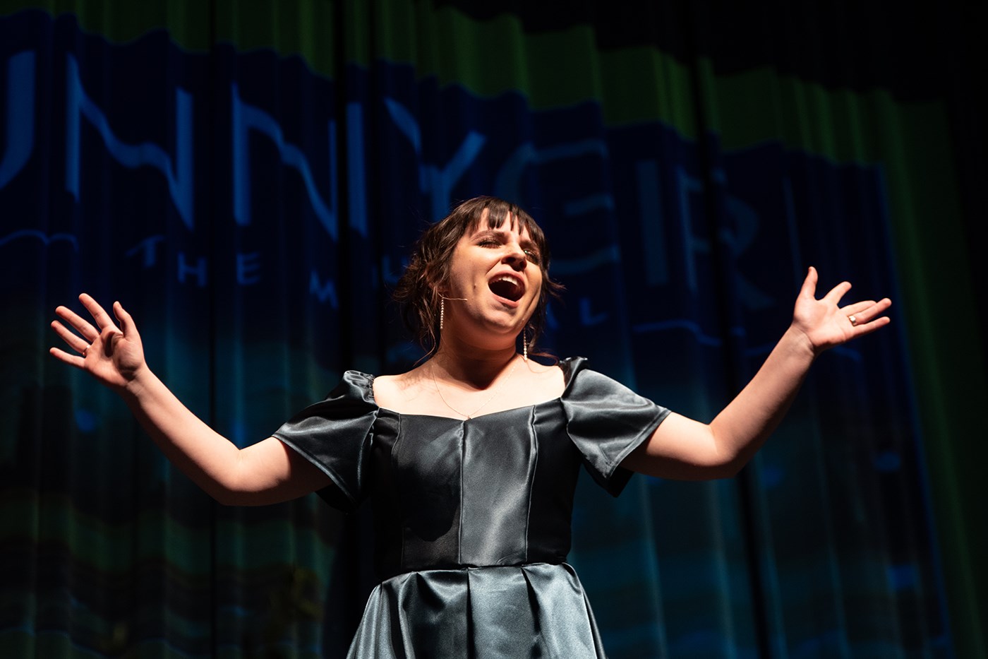 Young woman in a green dress singing a Broadway showtune