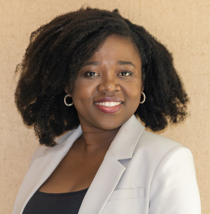 Gloria Donkor wearing a black shirt and white blazer coat and smiling at the camera.