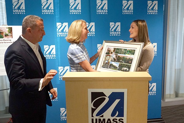 A woman in presented with a framed photo by another woman while a man looks on at a podium