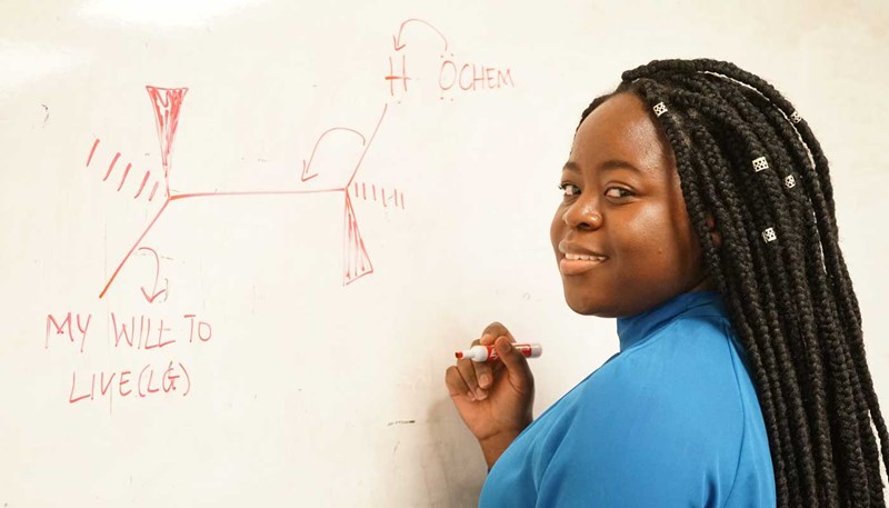 UMass Lowell biology student Dorcas Ruhamya stands at a whiteboard.