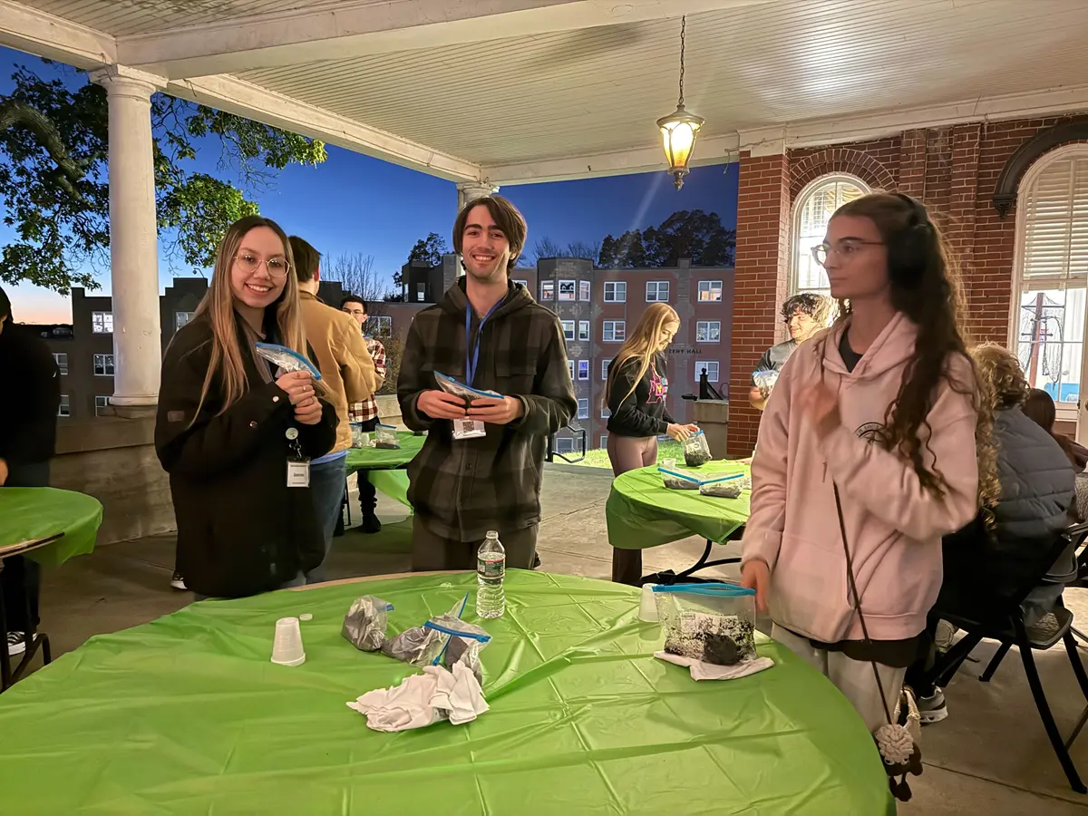 Students stand around table on back porch doing crafts.