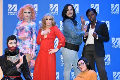 Six drag performers posing in front of a UMass Lowell backdrop